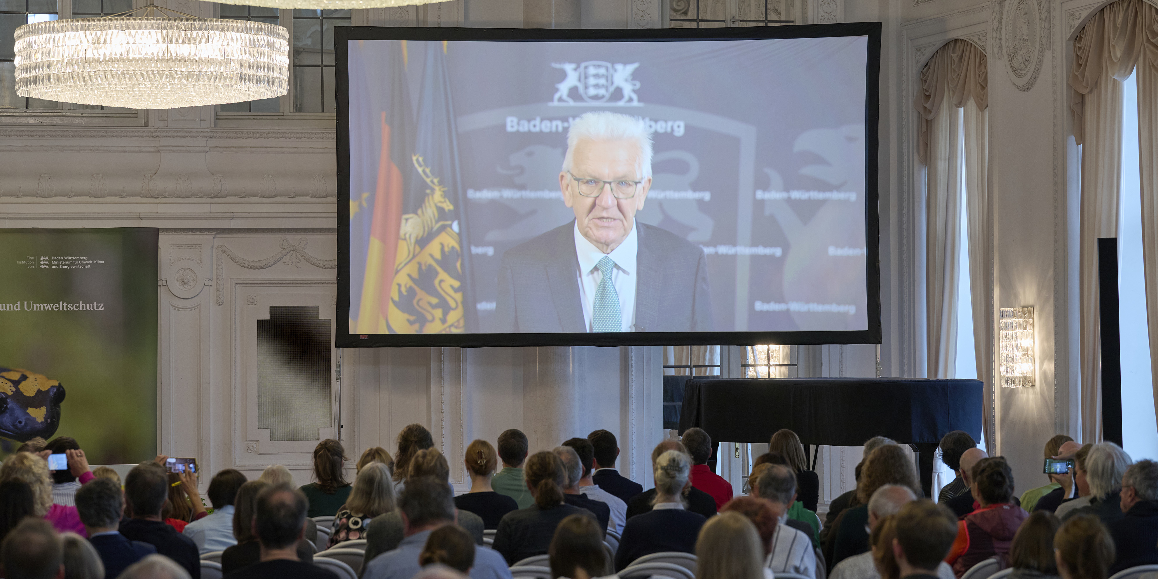 Ministerpräsident Kretschmann spricht zum Publikum über Video